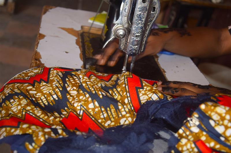Hands guiding Ankara cloth with red lightning bands through a sewing machine