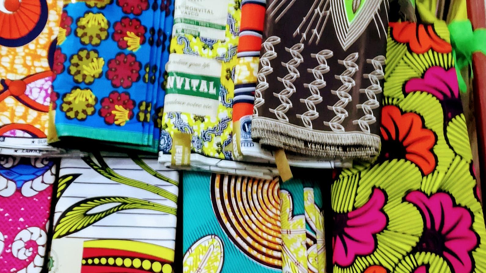 Stacks of folded wax prints in bright pinks, blues and yellows at a market stall