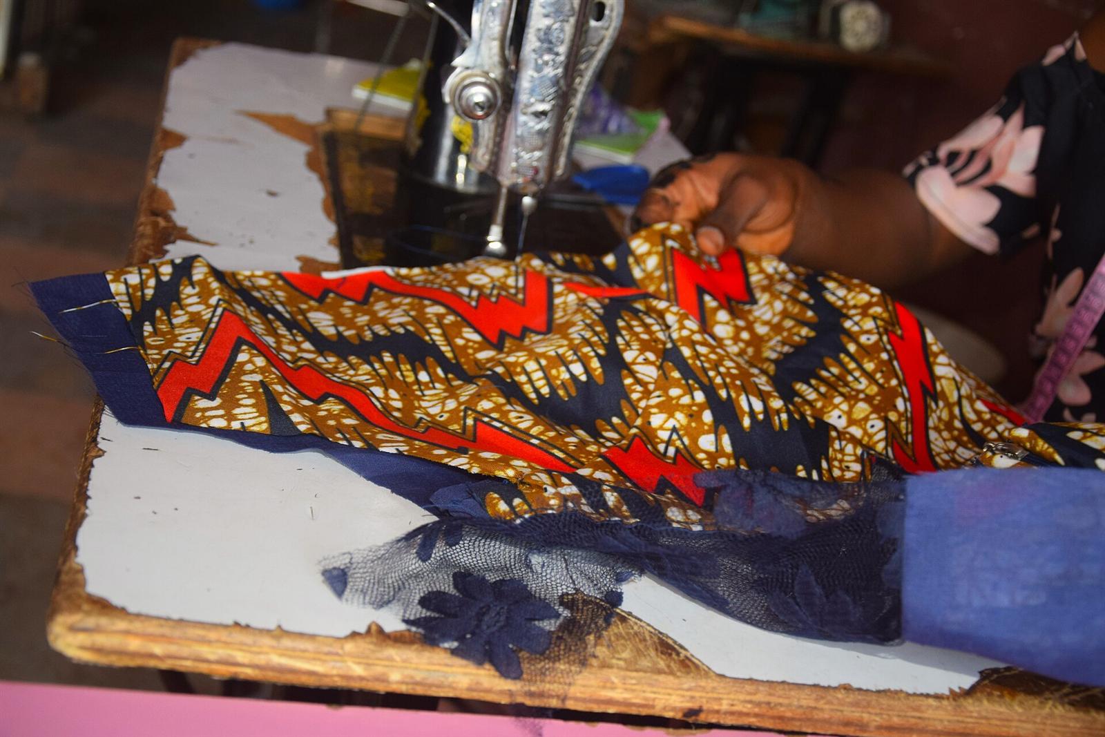 A tailor's hands feeding yellow, red and blue Ankara cloth under a sewing machine needle